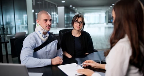 Worker wearing neck brace meeting with woman across desk in office