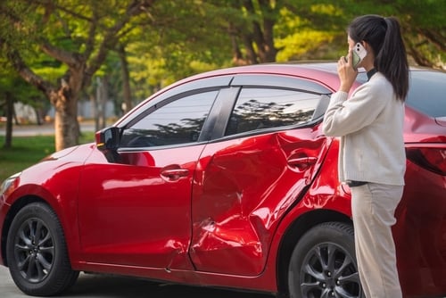 Woman covering face beside damaged car after traffic collision on roadway