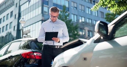Man holding clipboard between two cars during vehicle damage assessment