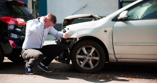 man crouching beside damaged vehicle holding neck after car collision