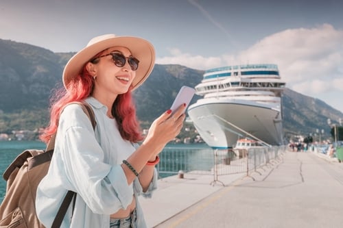young woman using smartphone on cruise ship dock wearing hat and backpack