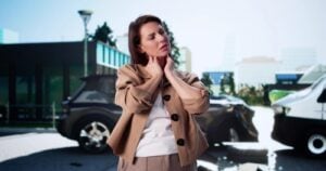 woman clutching neck in pain standing near damaged vehicles after collision