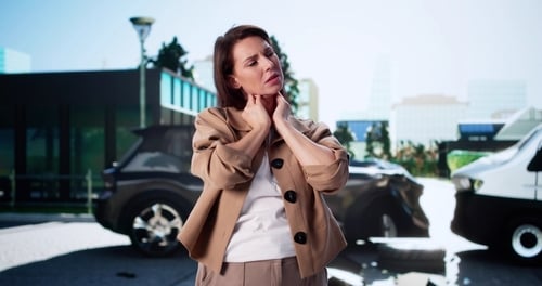woman clutching neck in pain standing near damaged vehicles after collision