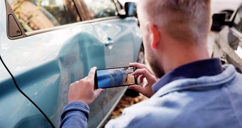man photographing vehicle door damage with smartphone after car accident